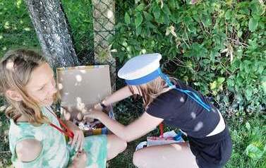 Fotografia przedstawia dwie dziewczynki, kt&oacute;re znajdują się na dworze i rozpakowują kartonowe puedełko.