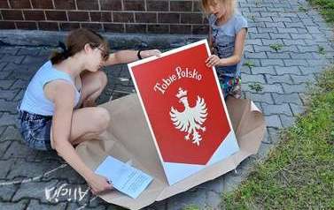 Fotografia przedstawia dwie dziewczynki, kt&oacute;re rozpakowują flagę powstańc&oacute;w śląskich. 