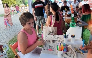 Warsztaty plastyczne podczas festynu. Dziewczynka koloruje torbę.