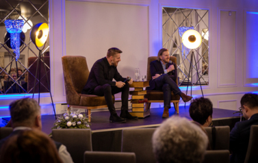 Szczepan Twardoch i Adam Zasada siedzą na fotelach. a przed nimi publiczność.